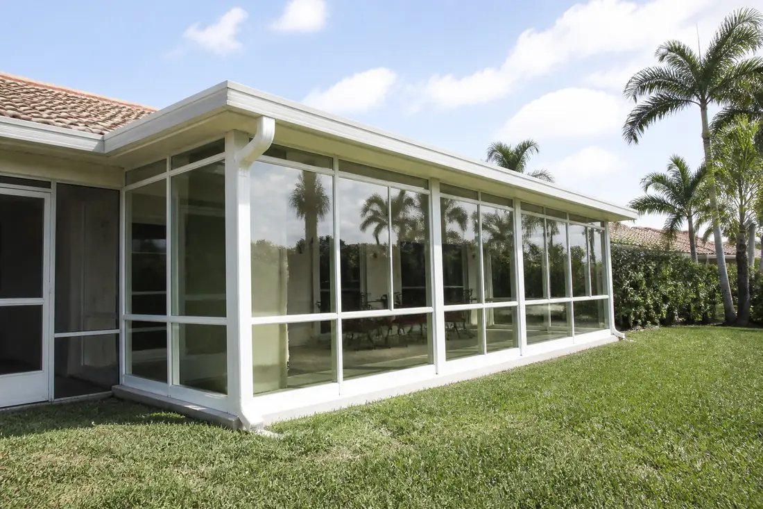 A glazed sunroom on the rear of a Southwest Florida house beside an older screened lanai