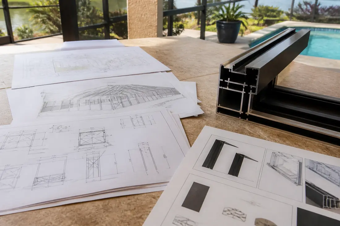 A stack of permit drawings and product documents on a table beside an aluminum enclosure frame section
